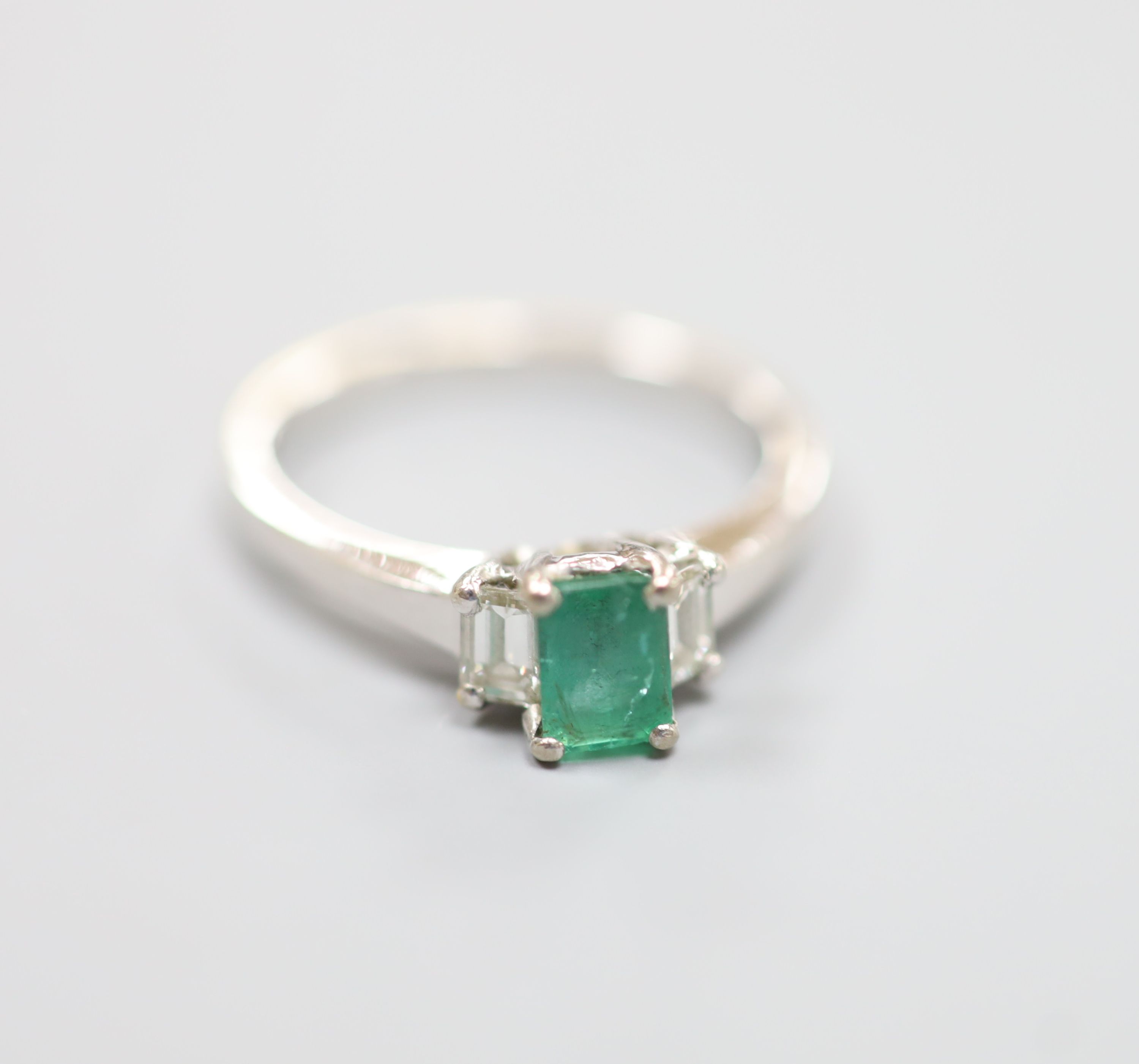 A modern white metal (engraved 750), emerald and diamond set three stone ring, size P